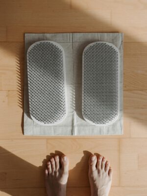 Person standing barefoot on acupressure mat for foot therapy, relaxing on a wooden floor.